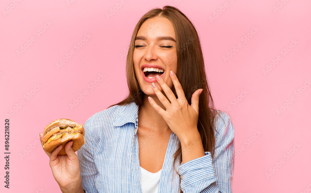 Junk Food. Young Woman Eating Burger And Laughing Standing Over Yellow Studio Background. Junk Food. Young Woman Eating Burger And Laughing Standing Over Yellow Studio Background.