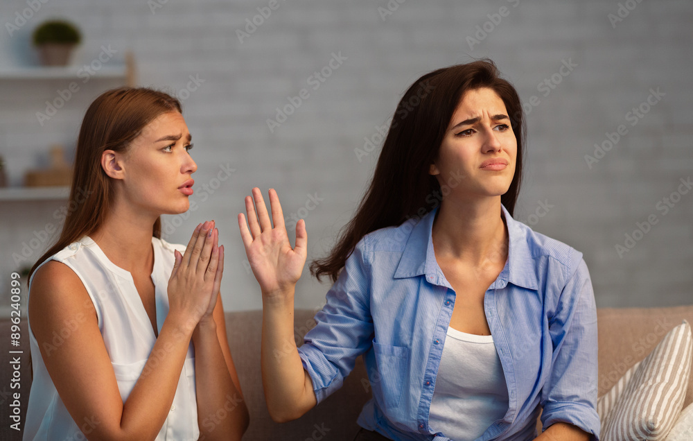 Φωτογραφία Miserable Girl Asking Indifferent Friend For A Favor Begging Holding Hands In Prayer Gesture Sitting On Sofa Indoor