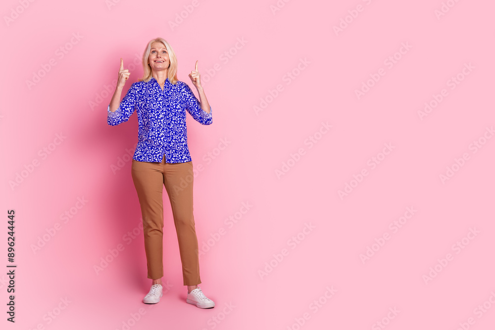 Full size photo of pretty aged lady direct fingers up empty space wear shirt isolated on pink color background Full size photo of pretty aged lady direct fingers up empty space wear shirt isolated on pink color background