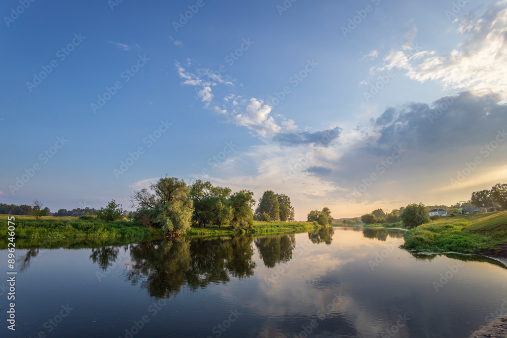 A calm river with trees on the banks and a cloudy sky in the background