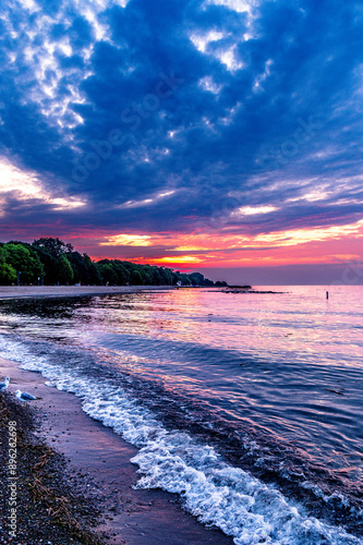 dawn over kew beach toronto witbn firey red orange and blue sky reflected in the water of lake ontario white foam at waters edge room for text photo