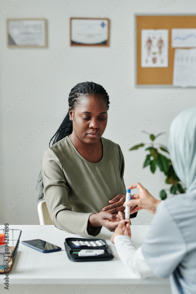 Young African American pregnant woman keeping hand over workplace of clinician checking her glucose level with digital medical device Young African American pregnant woman keeping hand over workplace of clinician checking her glucose level with digital medical device