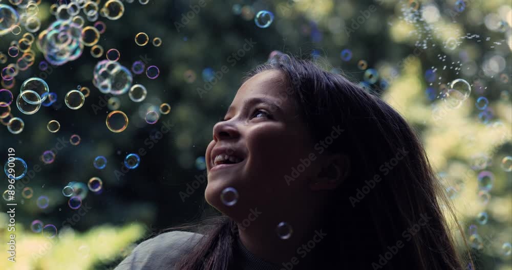 Smiling girl looking at bubbles floating around her in slow-motion at 800 fps, enjoying a whimsical and magical moment outdoors with a green background Smiling girl looking at bubbles floating around her in slow-motion at 800 fps, enjoying a whimsical and magical moment outdoors with a green background