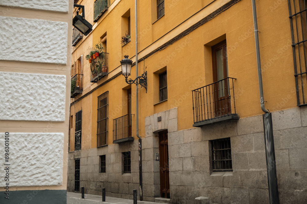 Naklejka premium Old narrow street downtown of Madrid with vintage buildings with small balconies decorated with potted flowers. Classic European architecture style