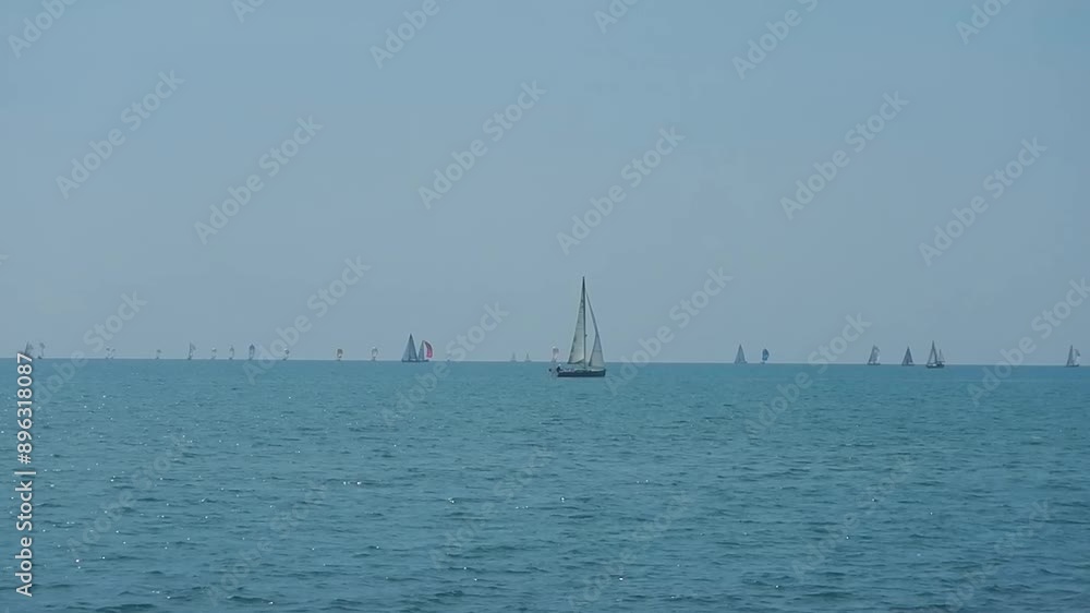 Sea with calm blue water surface with small waves, sunlight reflections, sailboats in distance and sky horizon with white clouds on sunny weather. Topics: holidays, rest, relaxation, seaside resort Sea with calm blue water surface with small waves, sunlight reflections, sailboats in distance and sky horizon with white clouds on sunny weather. Topics: holidays, rest, relaxation, seaside resort
