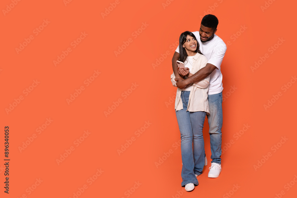 Couple Embracing and Looking Away, Standing Against Orange Background Couple Embracing and Looking Away, Standing Against Orange Background