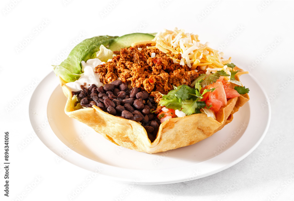 Fresh and healthy taco salad in a flour tortilla shell with black beans, avocado, ground chicken, lettuce, tomato, and cheese in a white plate on a white background; copy space Fresh and healthy taco salad in a flour tortilla shell with black beans, avocado, ground chicken, lettuce, tomato, and cheese in a white plate on a white background; copy space