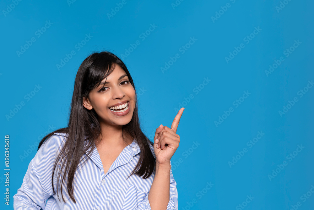 Smiling Woman Points Upwards Against Blue Background Smiling Woman Points Upwards Against Blue Background