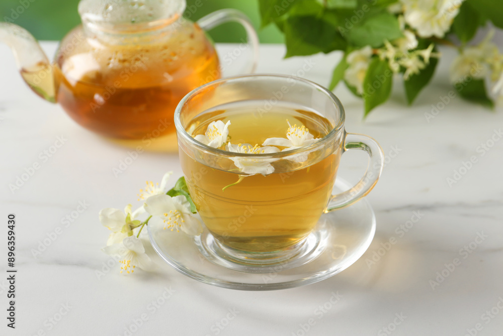Aromatic jasmine tea in cup, flowers, teapot and green leaves on white marble table Aromatic jasmine tea in cup, flowers, teapot and green leaves on white marble table