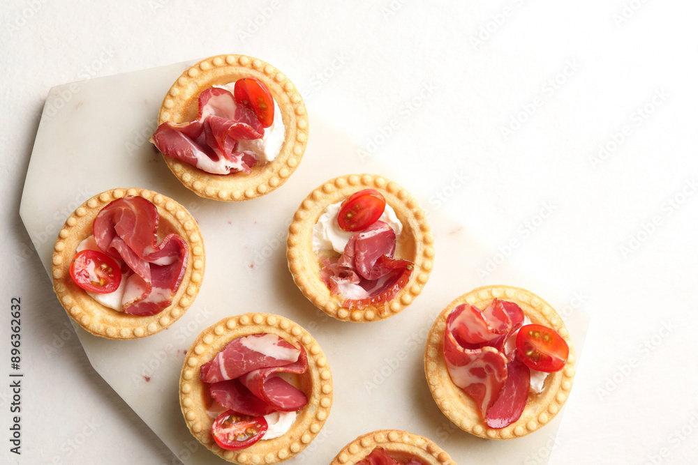 Delicious canapes with jamon, cream cheese and cherry tomatoes on white table, top view