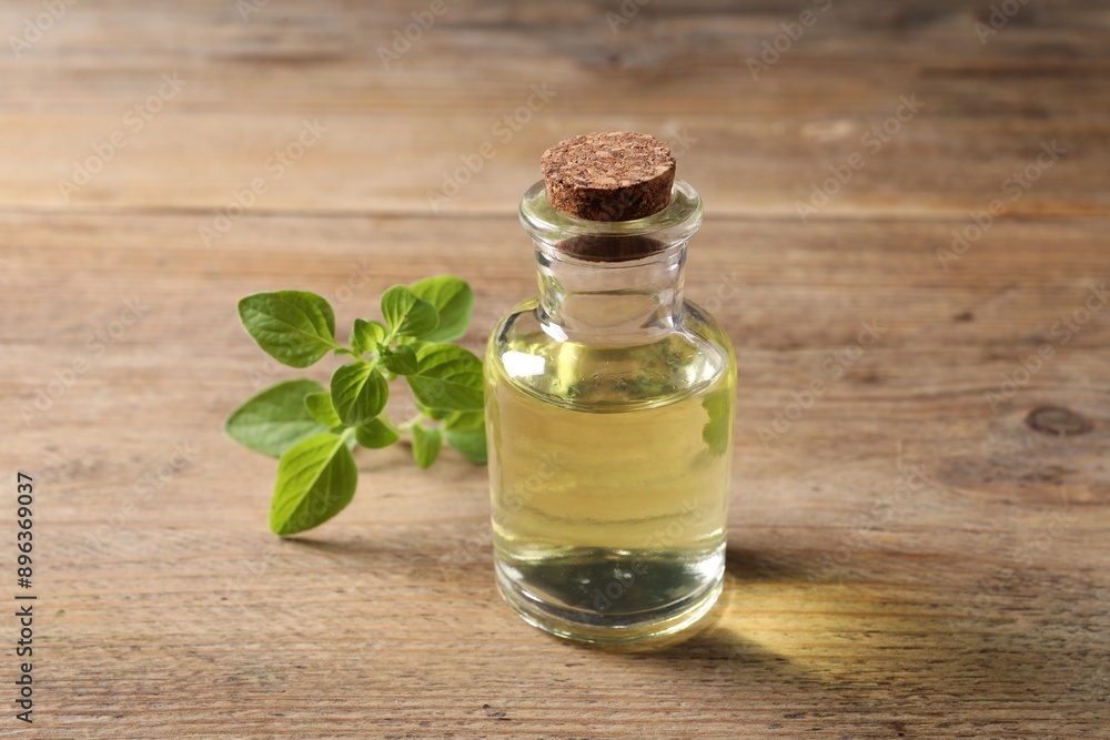 Essential oil in bottle and oregano twig on wooden table, closeup Essential oil in bottle and oregano twig on wooden table, closeup
