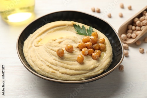 Delicious hummus with olive oil, chickpeas and parsley in bowl on white wooden table