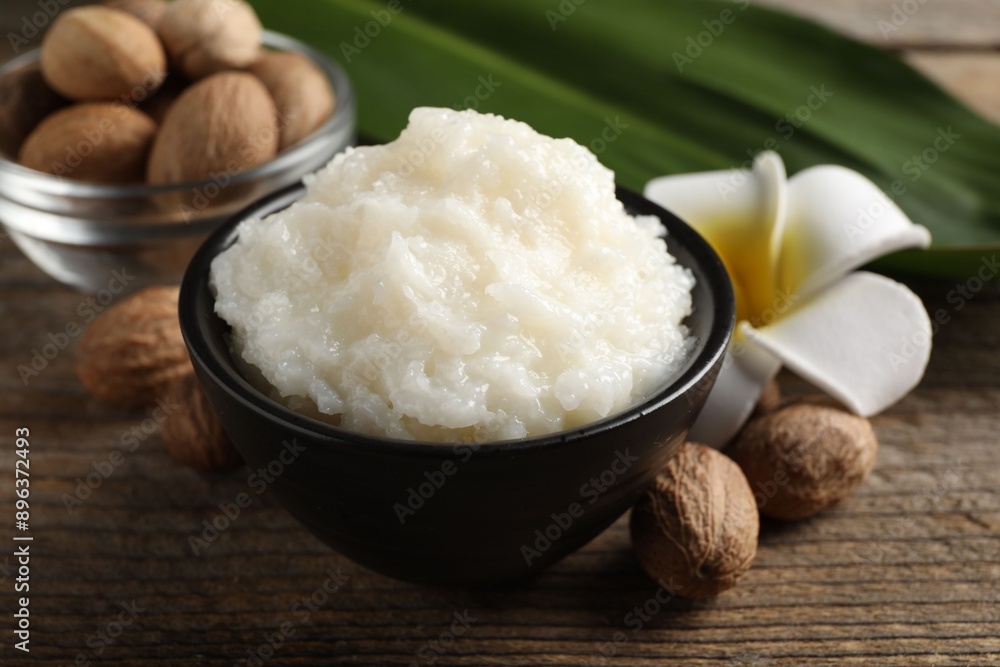 Natural shea butter in bowl, nuts and plumeria flower on wooden table, closeup Natural shea butter in bowl, nuts and plumeria flower on wooden table, closeup