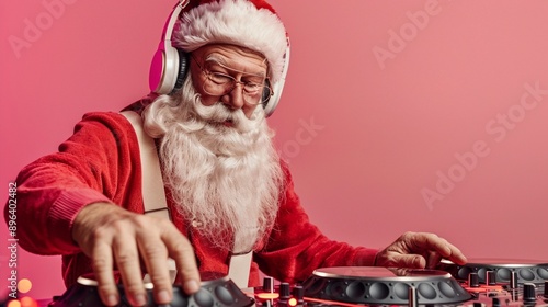 Modern Santa Claus in red suit and pink headphones mixing music on DJ turntables against vibrant pink background, blending holiday cheer with contemporary style. photo