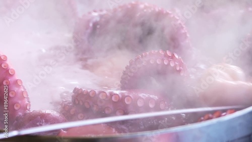 slow motion video of unrecognizable person stirring octopus being cooked in boiling water in a large restaurant pot