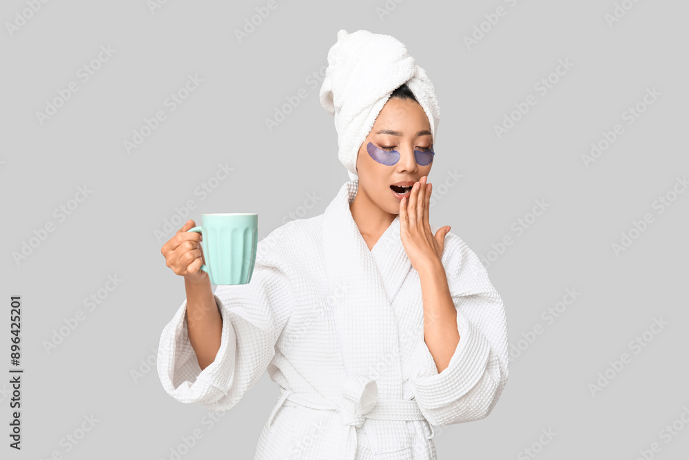 Sleepy young Asian woman with under-eye patches and coffee cup on light background Sleepy young Asian woman with under-eye patches and coffee cup on light background
