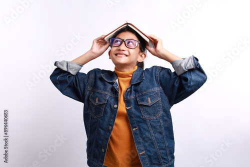 Happy asian school girl with a book on his head standing while thinking or imagine something. Isolated on white