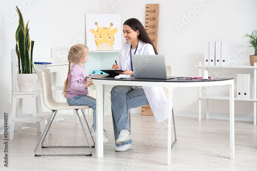 Female pediatrician working with little girl at table in clinic