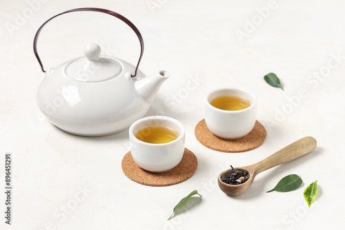 Teapot with cups, wooden spoon of dry tea and leaves on white background