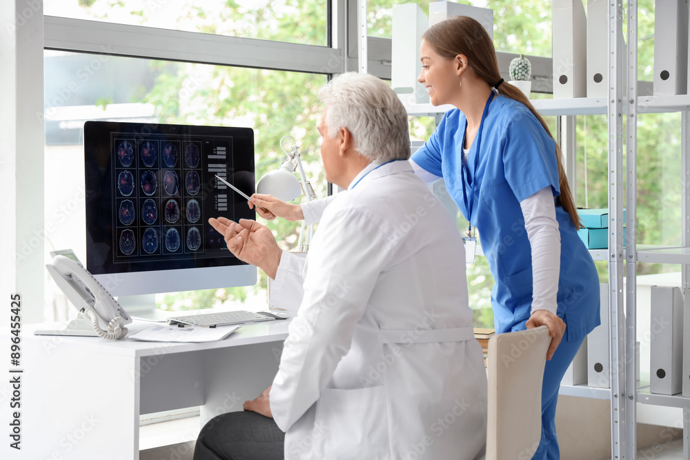 Mature doctor with nurse studying MRI scan on computer screen in clinic Mature doctor with nurse studying MRI scan on computer screen in clinic