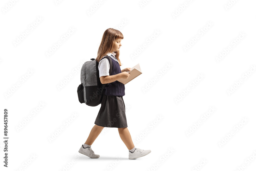 Full length profile shot of a schoolgirl in a uniform walking and reading a book Full length profile shot of a schoolgirl in a uniform walking and reading a book