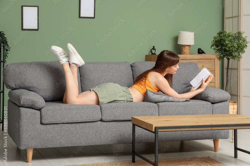 Beautiful young woman reading book on cozy sofa in living room Beautiful young woman reading book on cozy sofa in living room