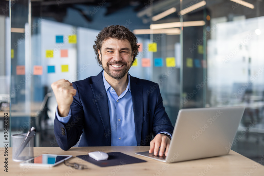 Joyful businessman in a modern office celebrating success with laptop. Handsome man in a suit cheering for a victory at work. Positive business environment and motivation. Joyful businessman in a modern office celebrating success with laptop. Handsome man in a suit cheering for a victory at work. Positive business environment and motivation.