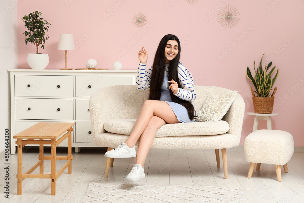 Pretty young woman sitting on white sofa in stylish living room Pretty young woman sitting on white sofa in stylish living room