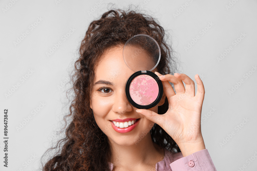 Beautiful young happy African-American woman with blush on grey background Beautiful young happy African-American woman with blush on grey background