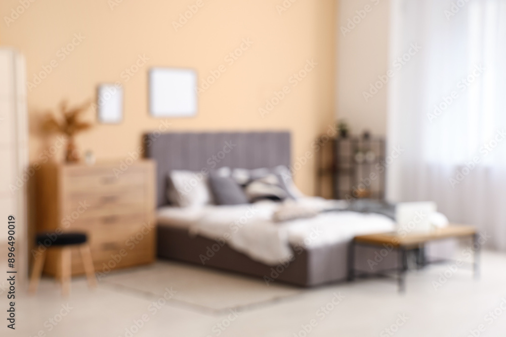 Fototapeta premium Comfortable bed, shelving unit, chest of drawers and bench in interior of bedroom. Blurred view