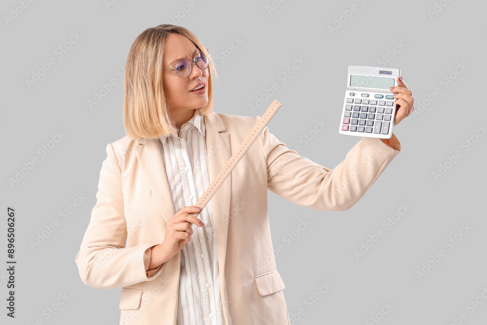 Mature female math teacher with ruler and calculator on grey background