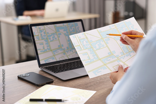 Cartographer working with cadastral maps at wooden table in office, closeup