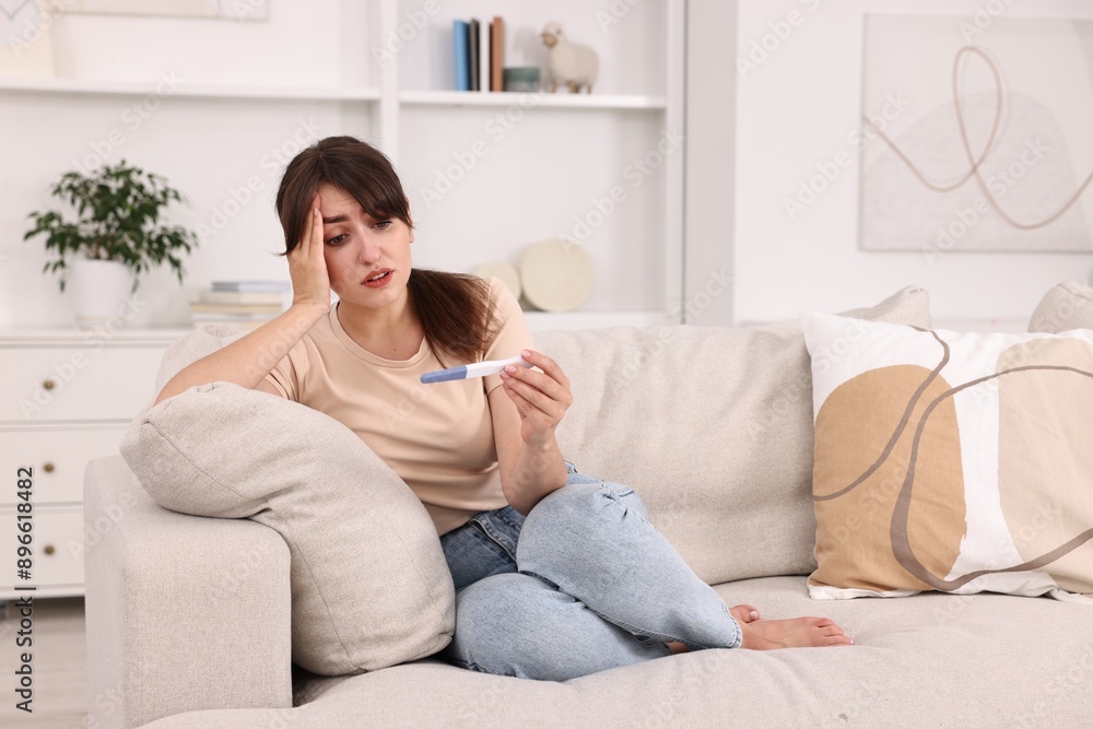 Worried young woman with pregnancy test on sofa at home Worried young woman with pregnancy test on sofa at home