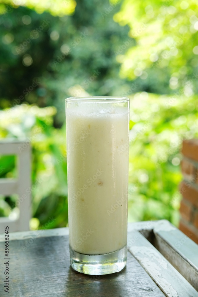 A refreshing glass of creamy banana smoothie placed on a rustic wooden table with a lush green background. Perfect for health and wellness blogs, summer refreshment promotions, and smoothie recipe A refreshing glass of creamy banana smoothie placed on a rustic wooden table with a lush green background. Perfect for health and wellness blogs, summer refreshment promotions, and smoothie recipe