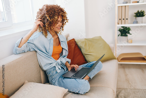 Smiling woman working from home, typing on laptop and enjoying her cozy living room