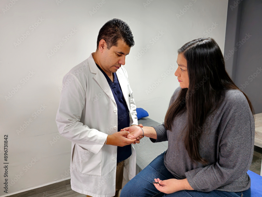Fototapeta premium Male brunette specialist doctor checks his latin woman patient suffering from pain in her hand due to injury, pain and deformity