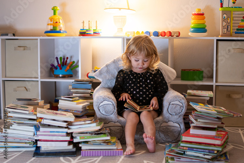 Little Caucasian blonde girl reading books in the evening. Little reader. Early Education concept. Baby and books