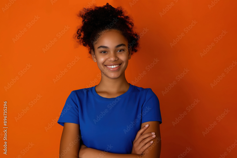 Young black woman in a blue t-shirt with crossed hands staying on the orange background and smiling Young black woman in a blue t-shirt with crossed hands staying on the orange background and smiling