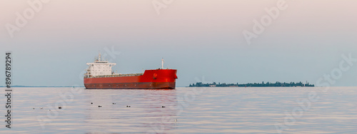 A large cargo ship moving in the water of the Black Sea. A red cargo ship is sailing on the sea.