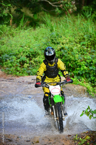 Motocross racing in the forest. One of the reacer in yellow racing suite riding his bike passing the waterway and mak it splash. photo