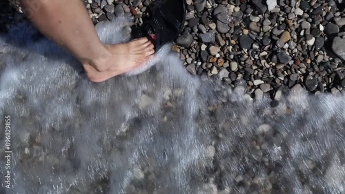 Lady with red toe nails sliding her foot in sandal on stoney Petoskey beach.