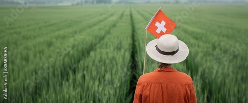 A person holding a Swiss flag, dressed in festive attire, standing on a lush green field during Swiss National Day photo