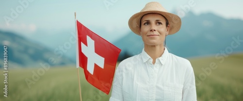 A person in festive Swiss costume with Swiss flag, posing in front of a clear blue sky and green fields photo