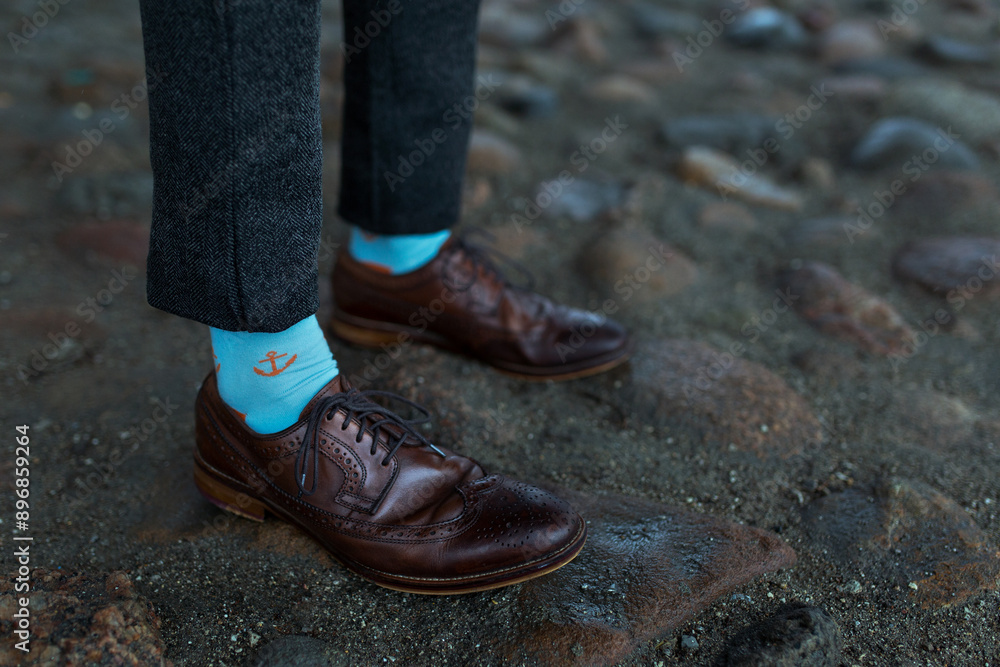 Person In Brown Leather Shoes With Blue Anchor Socks Stands On Cobblestone Path. Person In Brown Leather Shoes With Blue Anchor Socks Stands On Cobblestone Path.