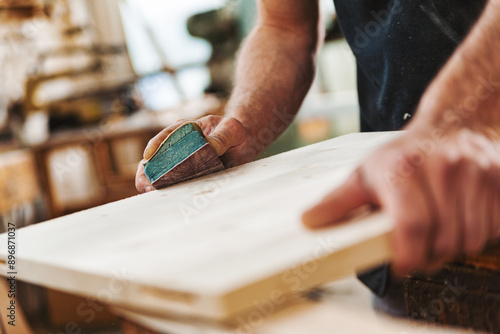 Carpenter sanding wood using sandpaper in workshop photo