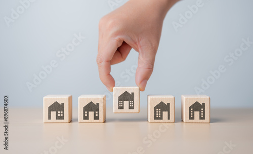 Real estate management, Property, Asset investment concept. Hand picking wooden cube block with house icon from others. Family makes the best decision when choosing the housing you truly want.