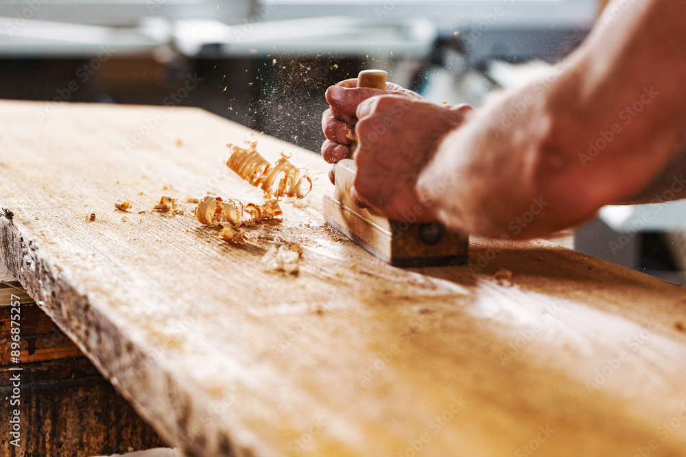 Carpenter using hand plane on wood plank in workshop Carpenter using hand plane on wood plank in workshop