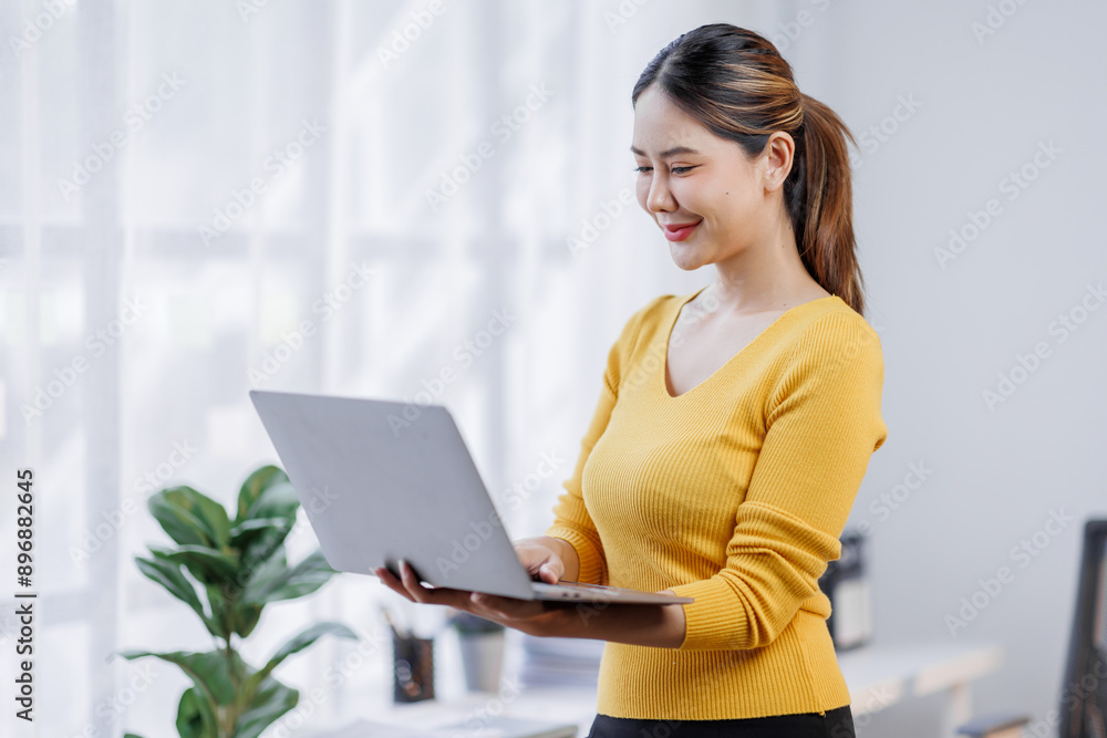 Portrait of young office asian woman, entrepreneur answer clients on laptop, working with computer with happy face, standing over in home office Portrait of young office asian woman, entrepreneur answer clients on laptop, working with computer with happy face, standing over in home office