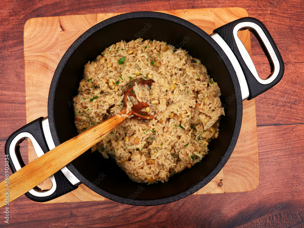 Iç pilav - Turkish rice with currants and pine nuts in a black pot, set on a wooden board, stirred with a wooden spoon Iç pilav - Turkish rice with currants and pine nuts in a black pot, set on a wooden board, stirred with a wooden spoon