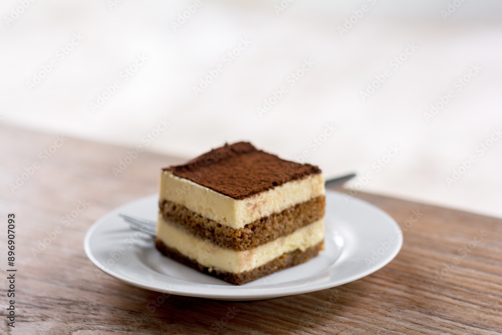 Close up a piece of tiramisu with mascarpone cream and biscuits on a white dish and wooden table..... Close up a piece of tiramisu with mascarpone cream and biscuits on a white dish and wooden table.....